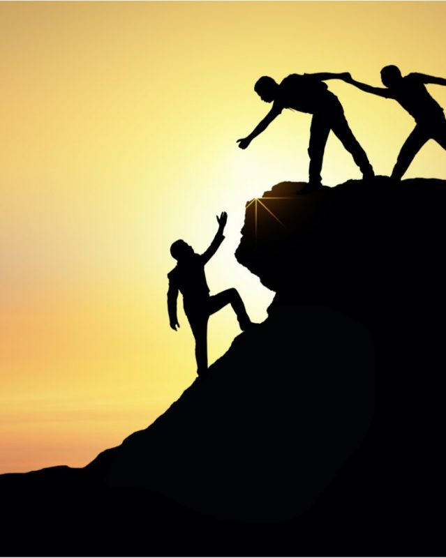 Two people helping another person climb a cliff
